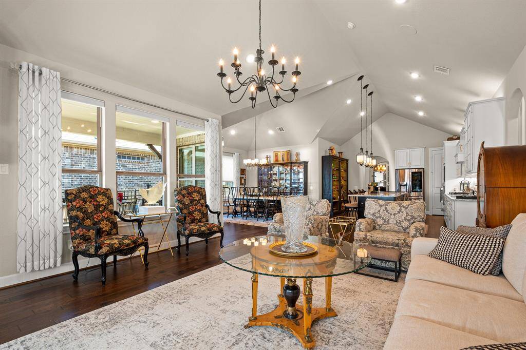 This elegant living space features high vaulted ceilings, and large windows for ample natural light. The open layout seamlessly connects to a Dining area and Kitchen, creating a warm and inviting atmosphere for entertaining.
