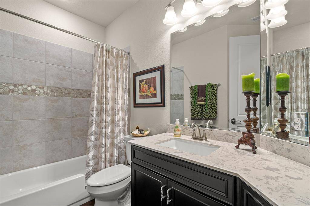 Secondary downstairs bathroom has a tiled shower and bathtub, quartz countertop, and dark wood vanity. It includes a large mirror, elegant lighting fixtures, and decorative accents, creating a stylish and functional space.