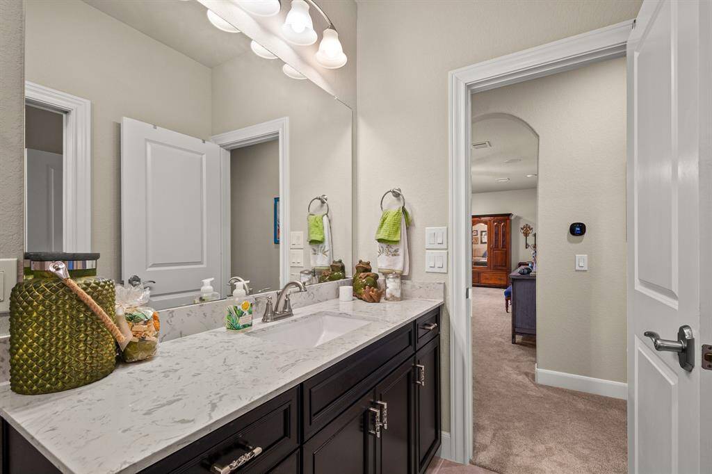 Discover the 3rd full bathroom with a sleek vanity, quartz countertop, stylish lighting, and ample storage. It connects seamlessly to a cozy, well-lit living area and Bedroom through the hallway.