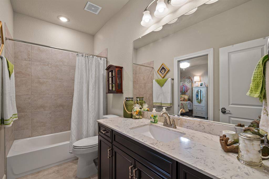 This elegant bathroom boasts a shower-tub combo, and ample lighting. Neutral decor with bright accents adds a touch of style, while an open door offers a peek into the adjacent bedroom.