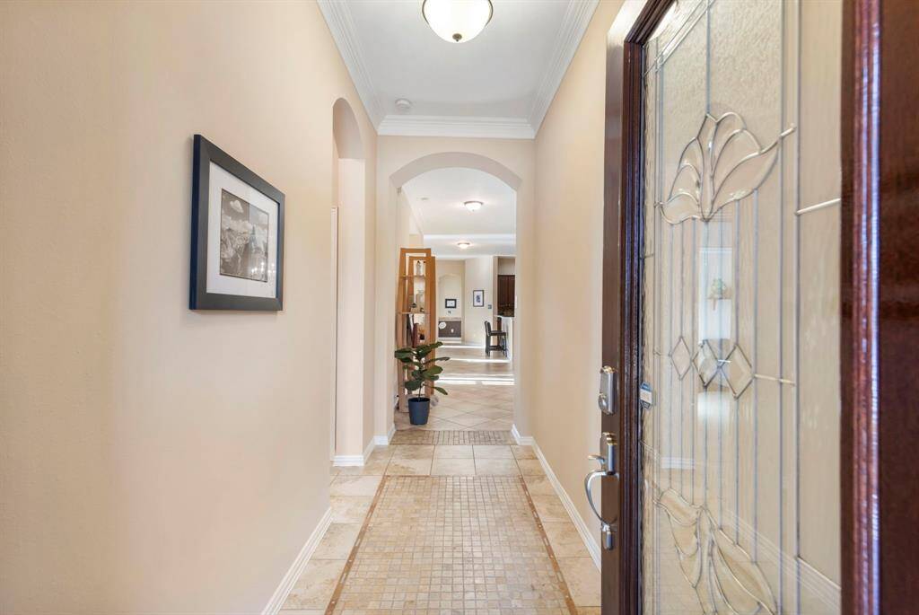 This welcoming entryway features a beautifully detailed glass front door, elegant tile flooring, and soft neutral walls. The hallway leads to a bright, open living space, accentuated by tasteful lighting and wall art.