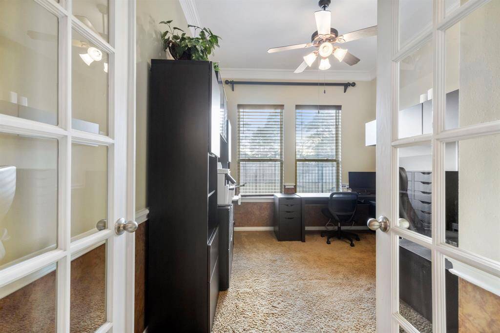This photo showcases a cozy home office featuring French doors, abundant natural light from large windows, and a ceiling fan.