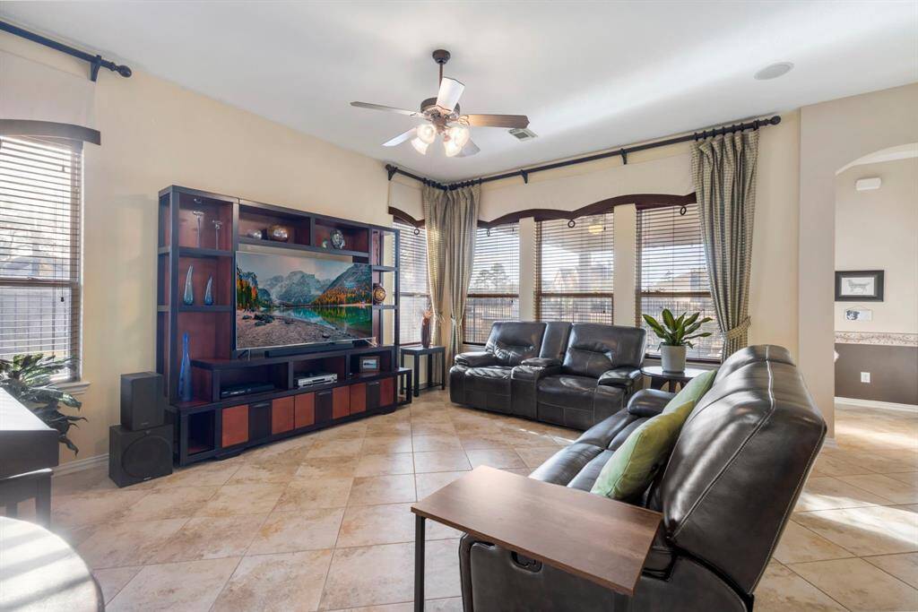 Bright and spacious living room with large windows, tiled floors, and a ceiling fan.