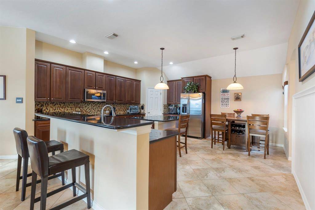 Spacious kitchen with dark wood cabinets, a sleek black countertop island with seating, and stainless steel appliances.