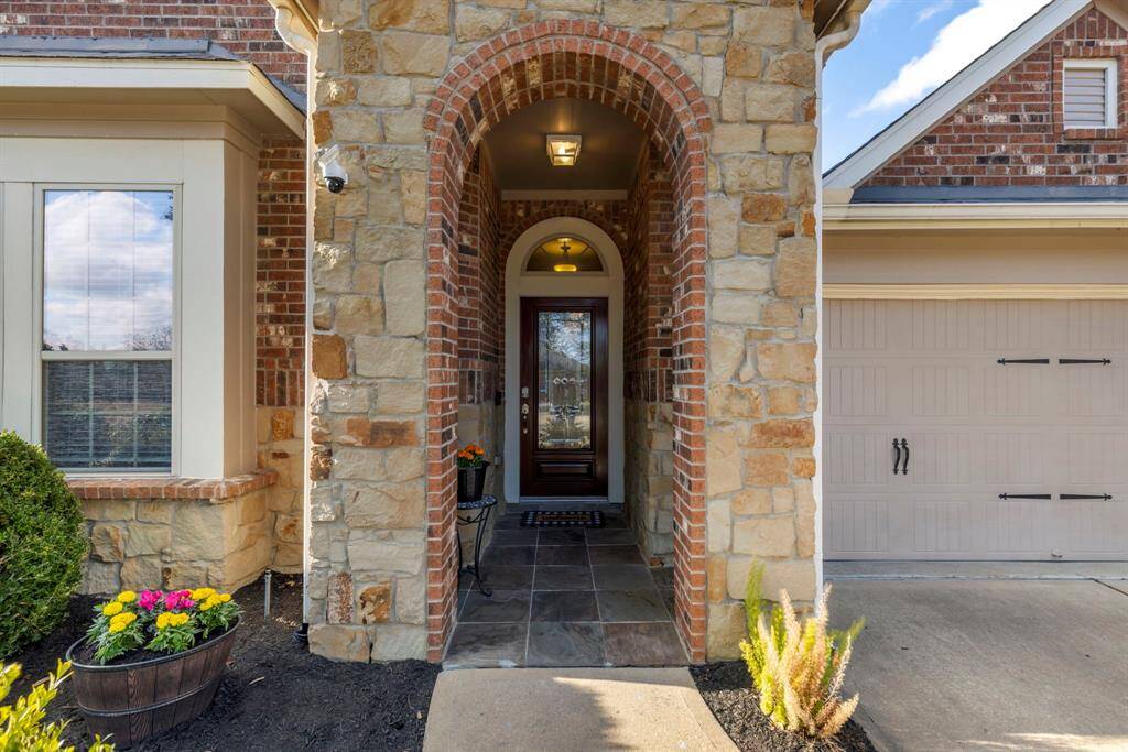 This inviting home features a charming front entrance with a stone and brick facade, an arched doorway, and a well-maintained garden. The wooden door with glass panels adds a touch of elegance, and the adjacent garage offers convenience.