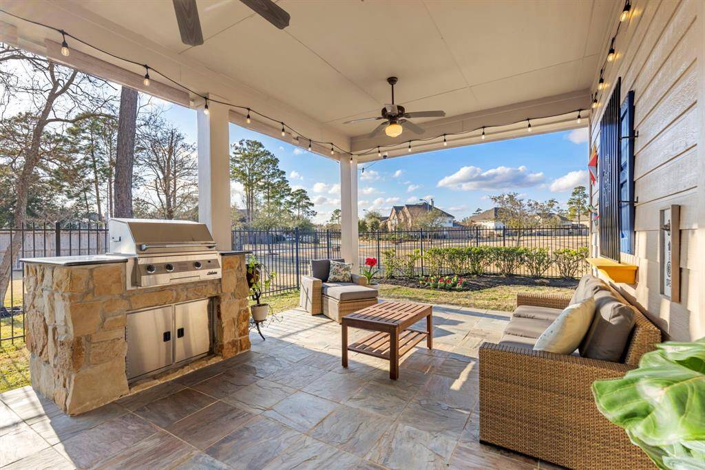 This photo showcases a charming outdoor patio with a built-in stone grill, cozy seating area, and ceiling fan. It's perfect for entertaining, with string lights adding a warm ambiance. The fenced backyard offers a scenic view.