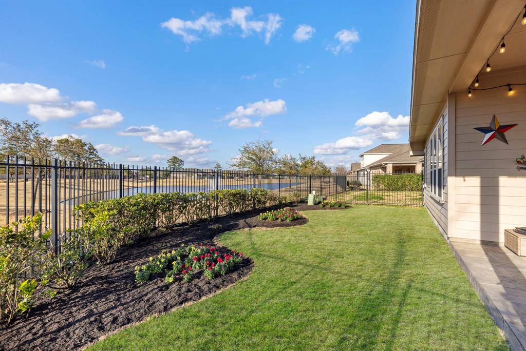 This photo showcases a well-maintained backyard with a lush lawn, flower beds, and a decorative star on the house. The yard is fenced with a view of open land, offering a spacious and peaceful outdoor area.