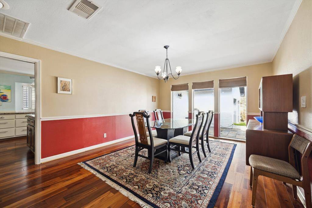 This elegant formal dining room features warm hardwood floors and a classic chandelier. The space includes large floor-to-ceiling windows that overlook the front patio offering a light and bright feel with easy flow to the kitchen.