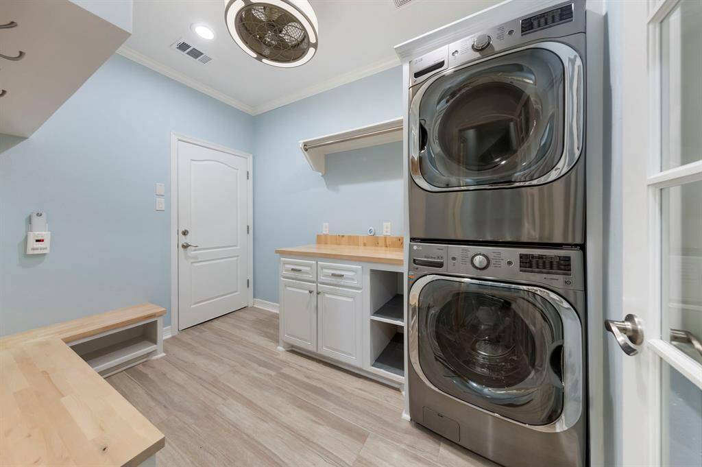 The redesigned utility/mud room features a stacked washer and dryer, complemented by countertop space and hanging racks, along with shoe storage and convenient garage access.