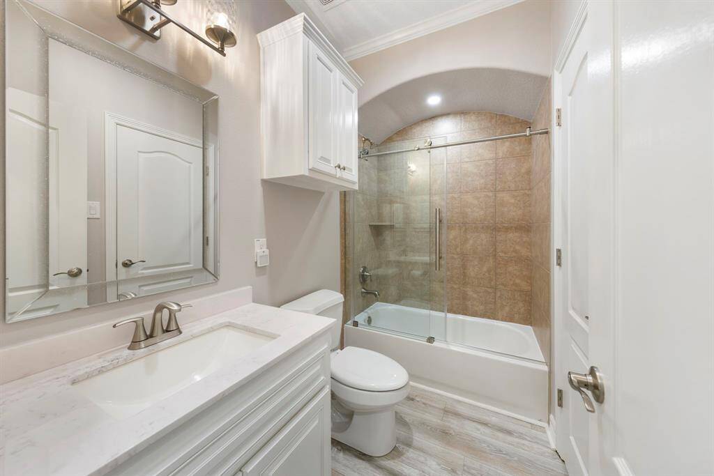 The second bathroom on the upper floor features a stylish tile shower/tub combo with a sliding glass door, modern white cabinetry, and a sleek vanity, blending functionality with contemporary design.