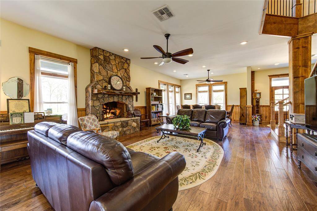 This spacious living room features warm hardwood floors, a cozy stone fireplace, and large windows for natural light with open layout perfect for family gatherings.