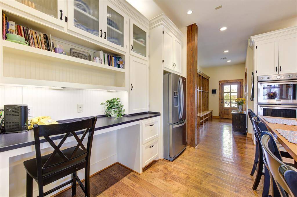 This kitchen features elegant white cabinetry with glass-front doors with a built-in desk area with ample storage and a Whirlpool french door stainless steel refrigerator.