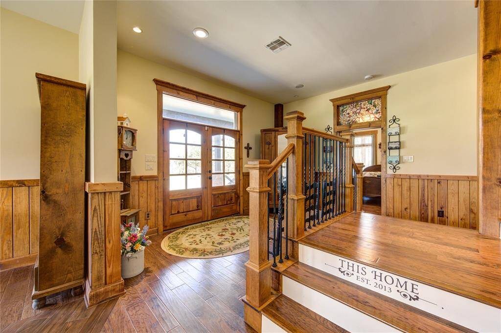 This welcoming entryway features warm wood accents and flooring, with a charming staircase leading to a restful, elevated area. The space is complemented by a large, glass-paneled double front door creating a rustic yet inviting atmosphere.