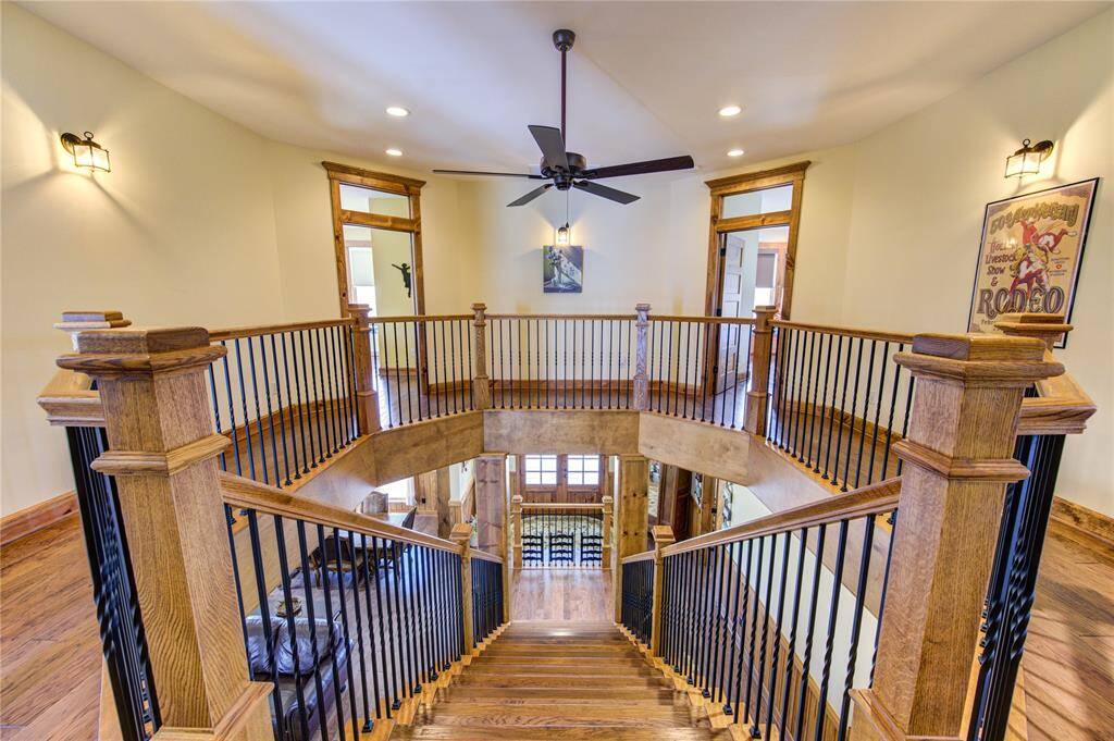 This spacious, elegant landing area with a wooden staircase featuring black metal railings. The space is well-lit with recessed lighting and wall sconces, and it includes a ceiling fan. This landing wraps around the entire landing for ease of traveling from room to room.