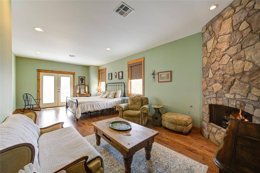The primary bedroom has a spacious layout with hardwood floors and a stone gas log propane fireplace. It includes a sitting area and large double doors for natural light. These double doors lead out to your very own private deck.