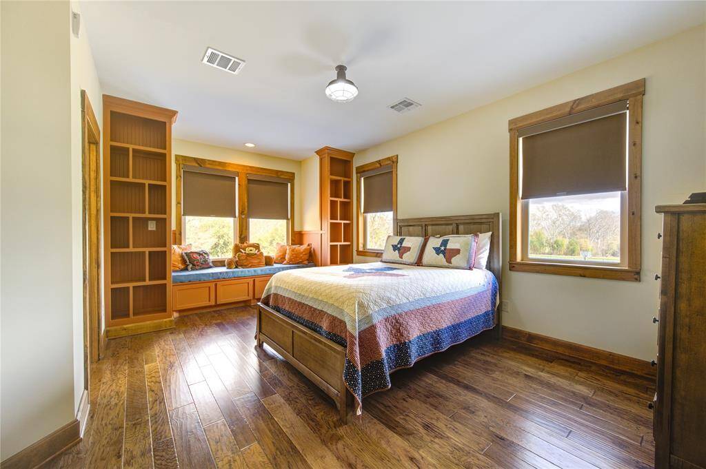 This secondary bedroom features hardwood floors and large windows with shades. It includes built-in bookshelves and a charming window seat with storage, offering a serene view of the outdoors.