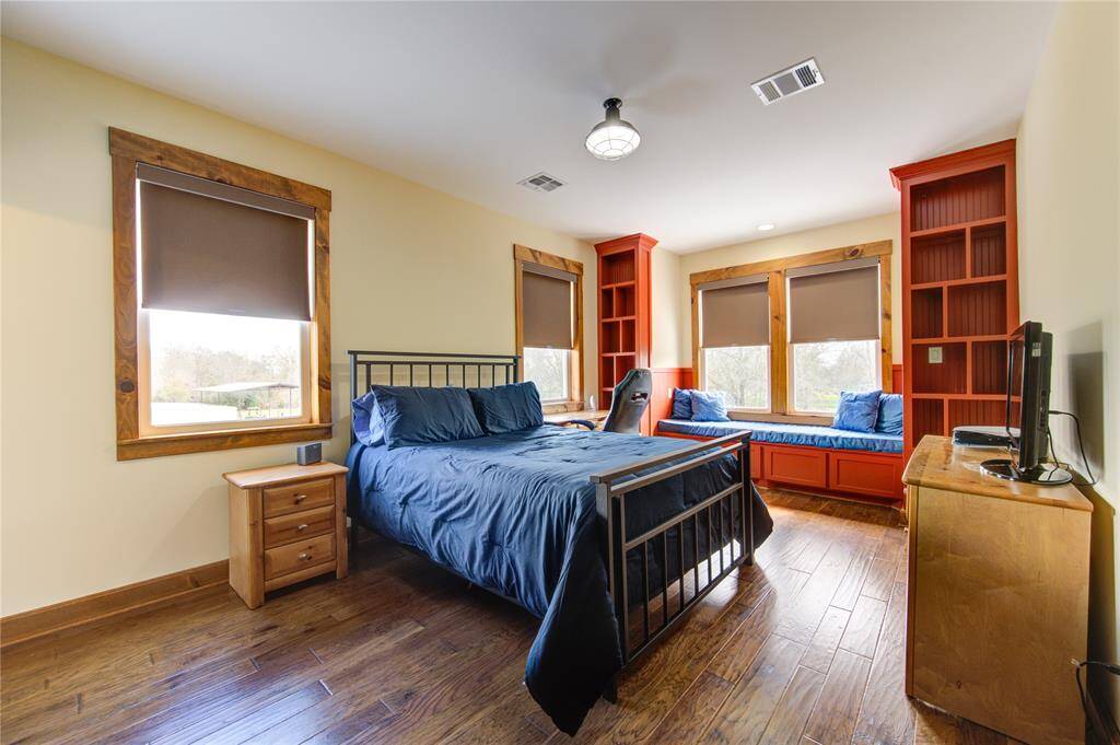 Another secondary bedroom features a wooden floor with lots of windows for natural light. It includes built-in shelving, a window seat with storage, and modern lighting, creating a warm and functional space. ALL bedrooms have an en suite bathroom.