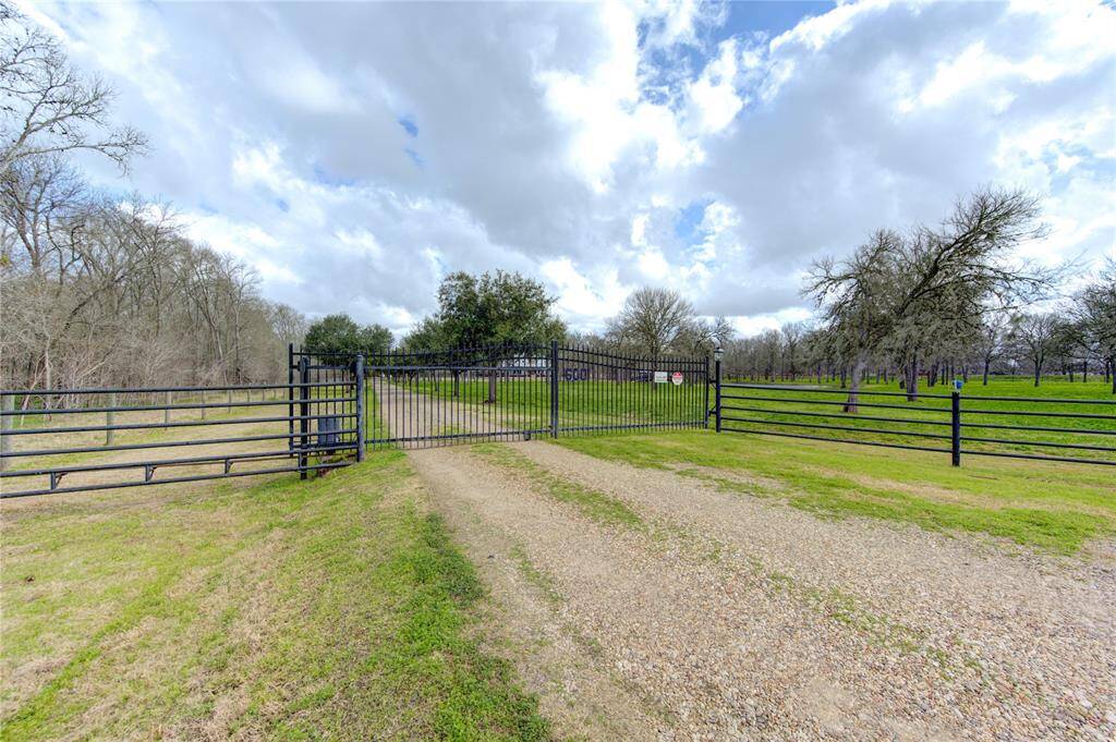 Welcome Home...the property's entrance with a gravel driveway and a black metal gate, surrounded by green fields and trees, creating a serene and private setting. This remote gated entrance is the only way onto the property adding an element of security to this pristine location.