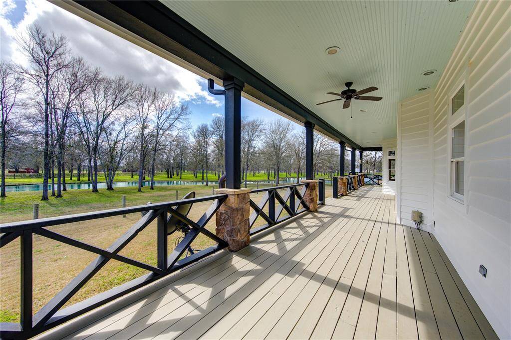 Spacious covered porch with ceiling fans, offering a serene view of a lush green yard and your own private pond, perfect for relaxing and entertaining.