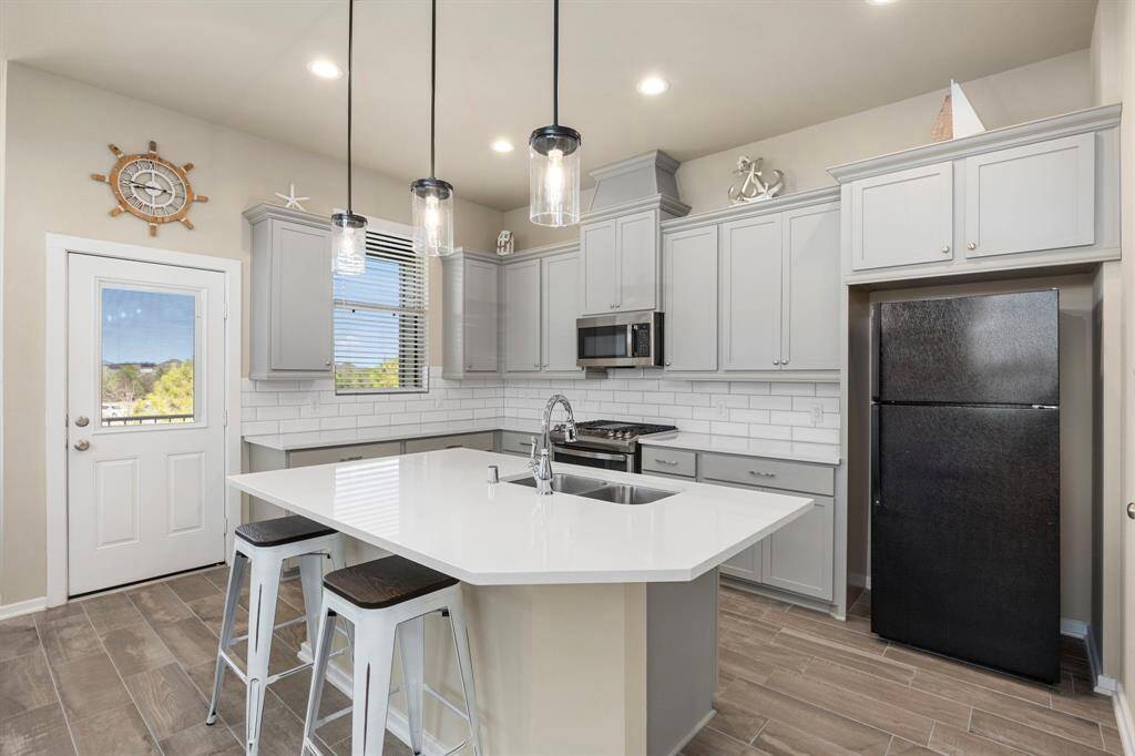 Luxury kitchen features white cabinetry, SS appliances, quartz counters, subway backsplash, bar, and pendant lighting.