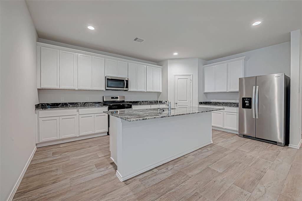 Home kitchen boasts large island, elegant granite countertops, shaker-style cabinetry, and sleek stainless-steel appliances, including a gas range, dishwasher, and microwave hood combo.