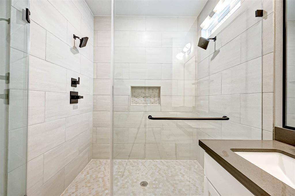The primary bath shower has tile surround, stone tile mosaic floor, and custom hardware.