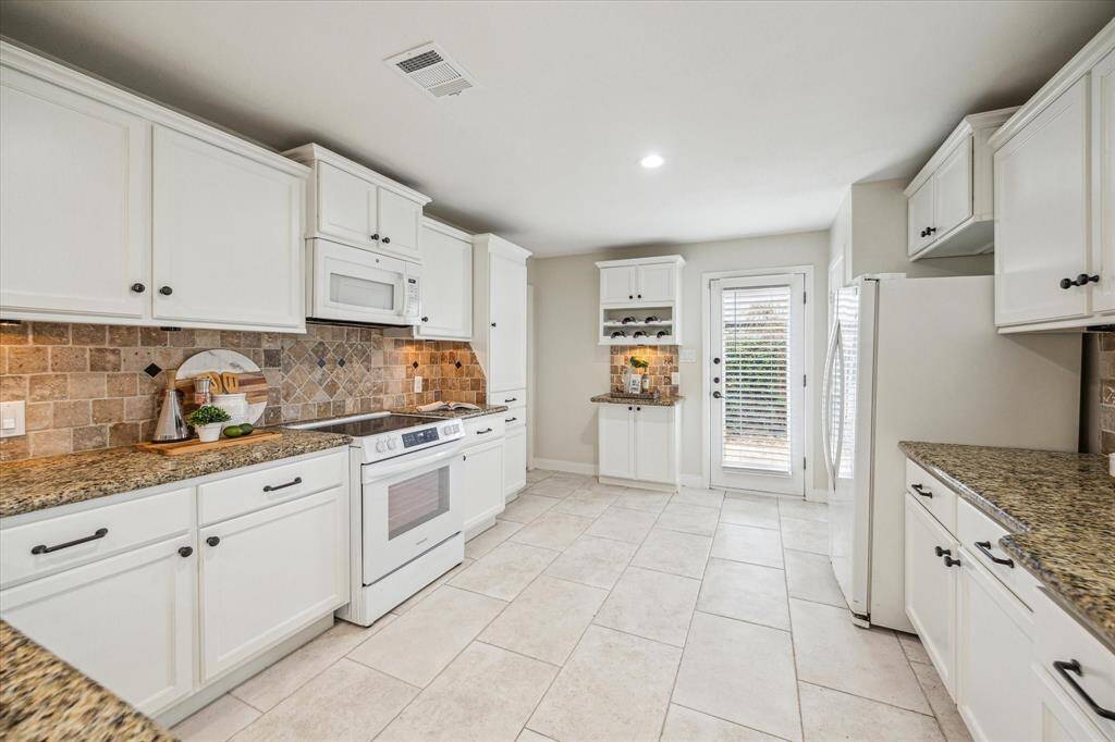 This fully loaded kitchen has it all! Find crisp white cabinetry with modern pulls, sleek granite countertops, under-cabinet lights, tumbled stone backsplash, built-in appliances and plenty of room for the sous chef and cleanup crew.