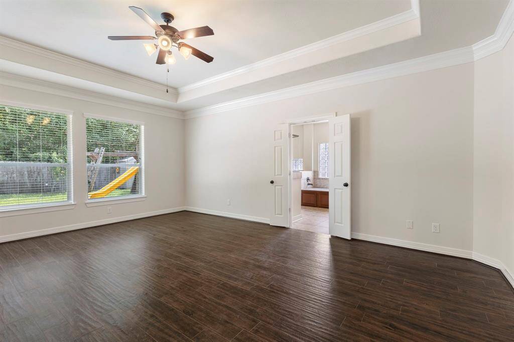 The primary bedroom is elevated by a tray ceiling with double crown molding, wood-looking tile floors and backyard views of the greenbelt.