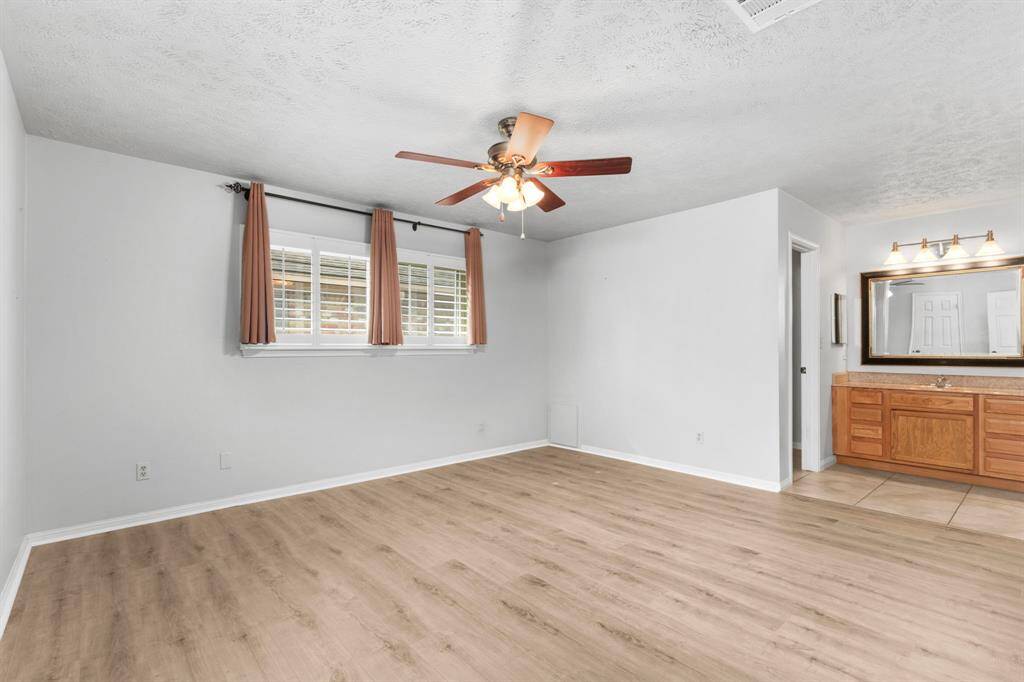 Primary bedroom, vinyl plank flooring, two closets, plantation shutters, ceiling fan with light, private tub/shower combo with tile surround and vanity just outside.