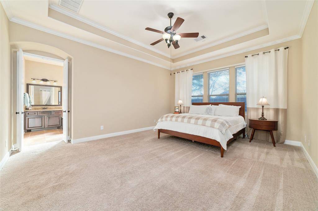 Primary bedroom with tray ceilings for depth, ceiling fan, and wall of windows