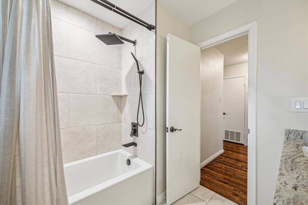 The guest bathroom features a fully tiled soaking tub/shower enclosure with crisp clean tile, a shampoo ledge, and sleek modern fixtures.