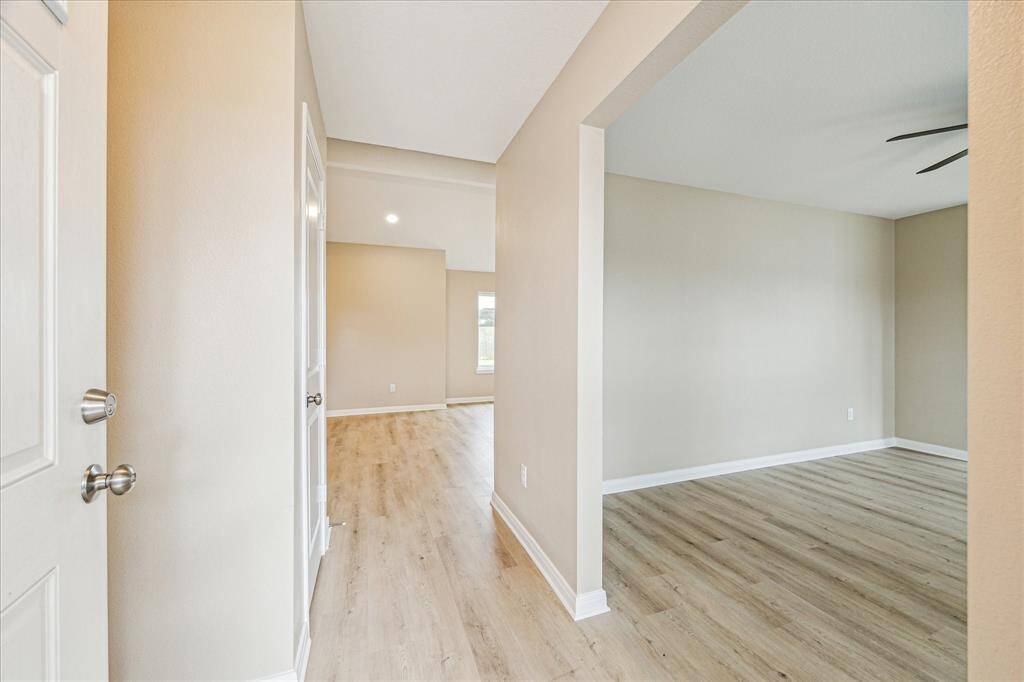 This photo shows a bright entryway with light vinyl wood flooring, neutral walls, and an open layout that leads to additional rooms, creating a welcoming and spacious atmosphere.