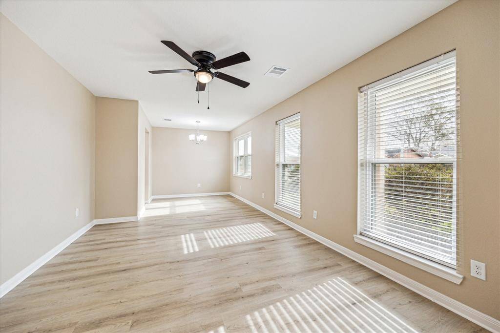 Bright and spacious formal living and dining room with light wood flooring, neutral walls, and large windows allowing ample natural light. Features include a ceiling fan and a stylish light fixture, perfect for entertaining.