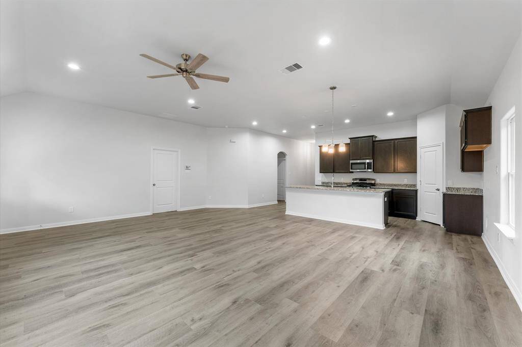 This photo showcases a spacious, open-concept living area with modern luxury flooring and neutral walls. The kitchen features dark cabinetry, granite countertops, and stainless steel appliances. A ceiling fan and recessed lighting provide comfort and illumination, creating a bright and welcoming space.