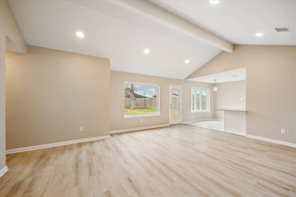 This open-concept family room features light wood flooring, neutral walls, and recessed lighting. It offers ample natural light with large windows and a door leading to the backyard. The space seamlessly connects to kitchen breakfast area and kitchen with a modern layout.