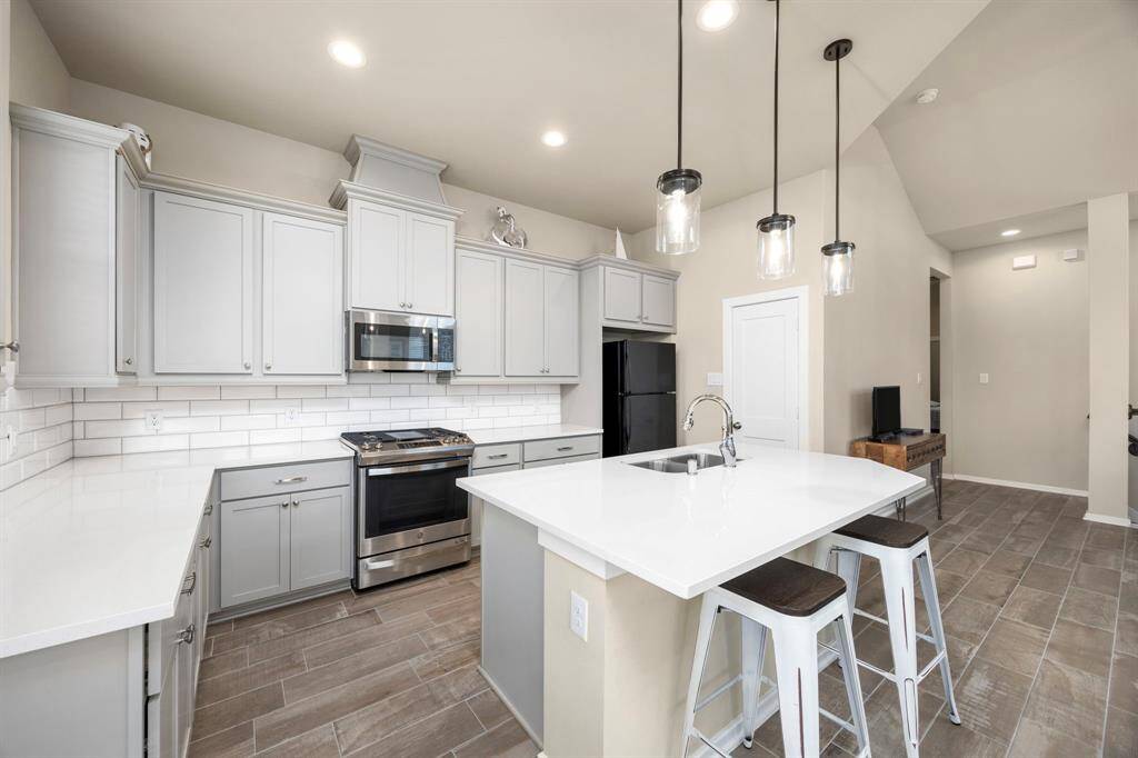 Luxury kitchen features white cabinetry, SS appliances, quartz counters, subway backsplash, bar, and pendant lighting.