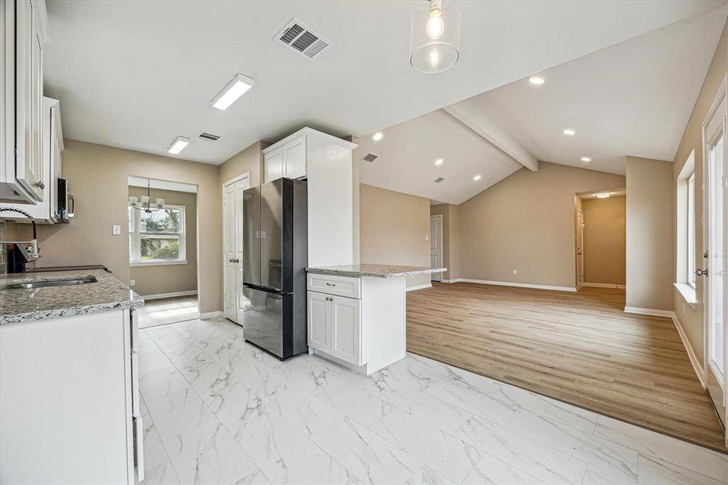 This photo showcases a modern, open-concept kitchen and family area.  It transitions seamlessly into a spacious family room with high ceilings and vinyl wood flooring, creating a bright and inviting space.