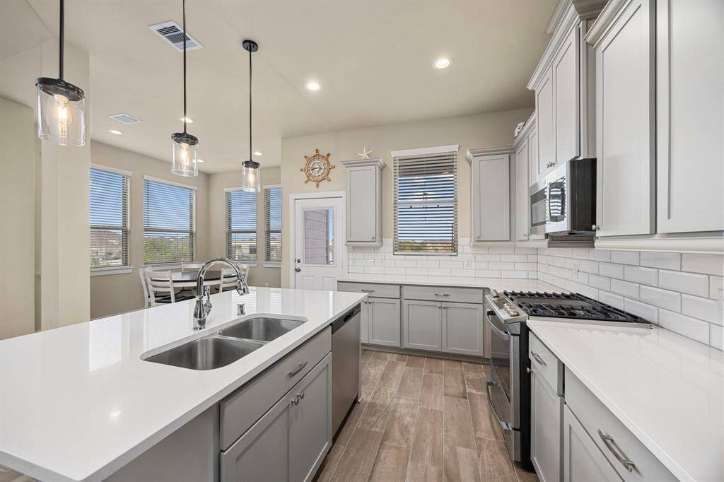 Luxury kitchen features white cabinetry, SS appliances, quartz counters, subway backsplash, bar, and pendant lighting.