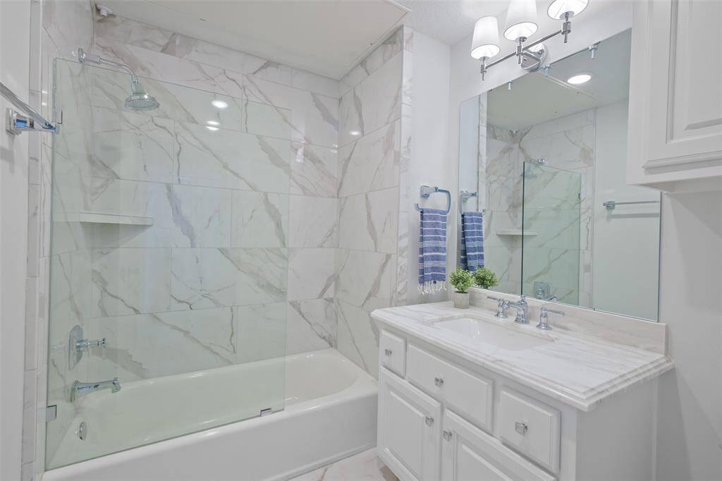 A closer view of the tub and shower combo with custom glass door and updated vanity; walk-in closet just outside the door.