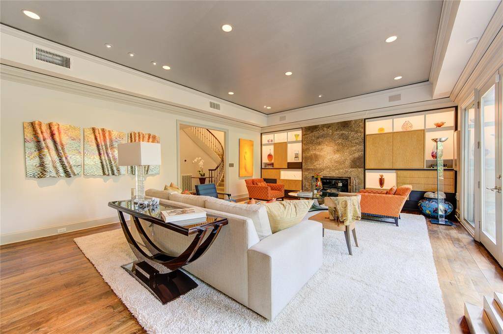 This spacious living room features modern decor with built-in shelving for art display, a historic marble surround fireplace, French style doors to the most spectacular views of the bayou ravine. It boasts ample natural light from large windows, complemented by elegant lighting fixtures and a soft color palette. Perfect for entertaining or relaxing.