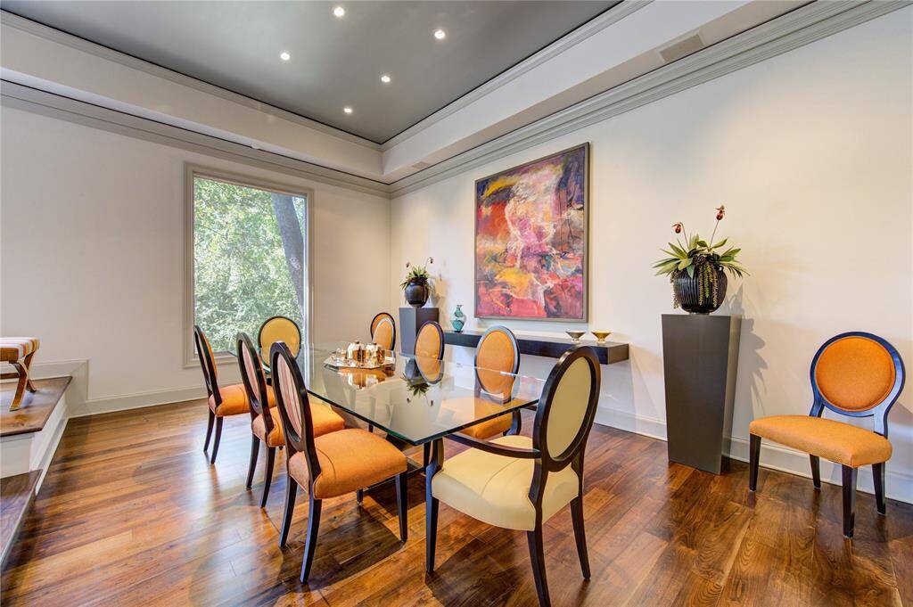 This elegant dining room features spaces for all of your guests. The room has high ceilings and  is well-lit with recessed lighting and a large window offering natural light and a scenic view. Rich wooden flooring adds warmth and sophistication.