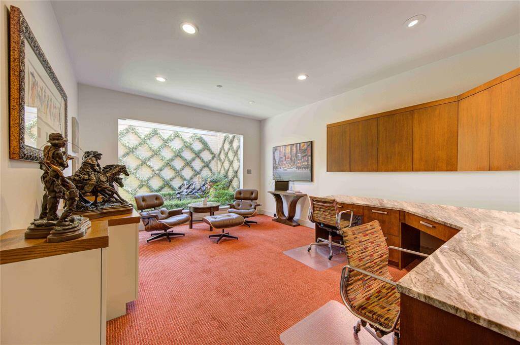 Spacious home office with a modern design. It features a large window providing natural light and a view of greenery in a private courtyard. The room includes built-in wooden cabinetry and a marble-topped desk, creating an inviting workspace. This room can also be utilized as a 4th bedroom if needed.