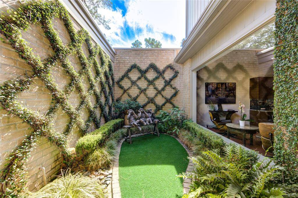 Charming, enclosed courtyard with lush greenery and vines adorning the walls. It features artificial grass, and an open connection to an indoor space, creating a seamless indoor-outdoor living experience. (art sculpture not included)