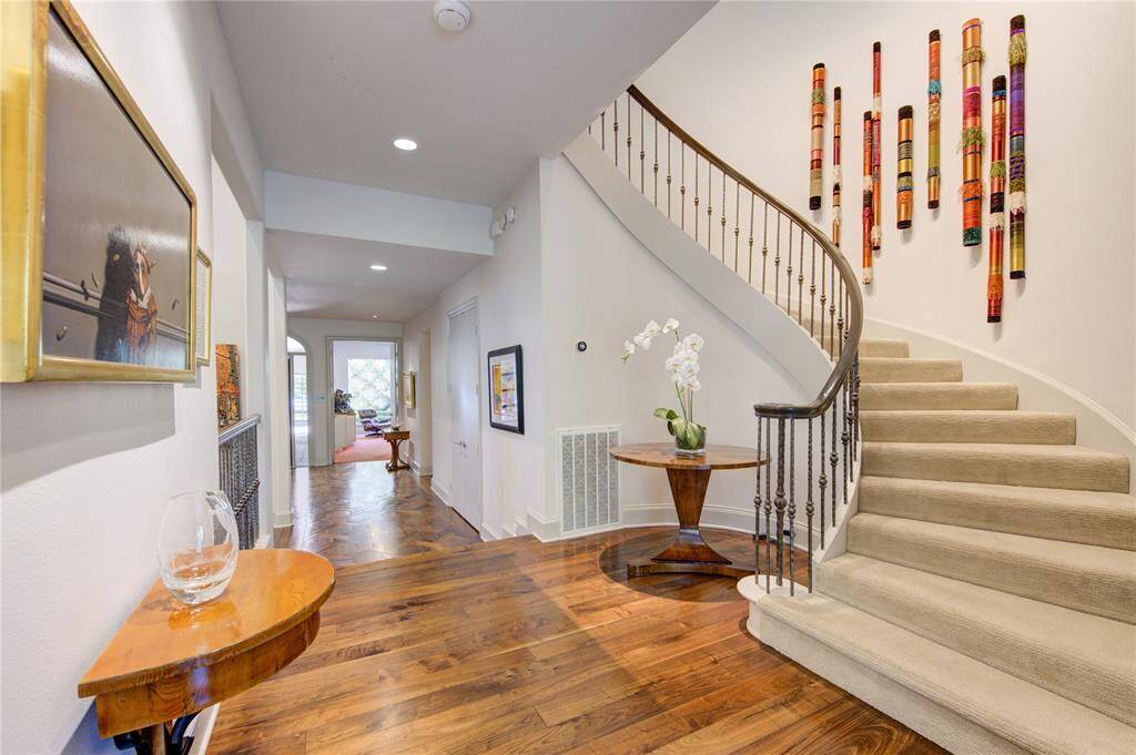 Inviting foyer features a wide curved staircase with elegant railings and another great wall for art. The space is accentuated by hardwood floors and recessed lighting.