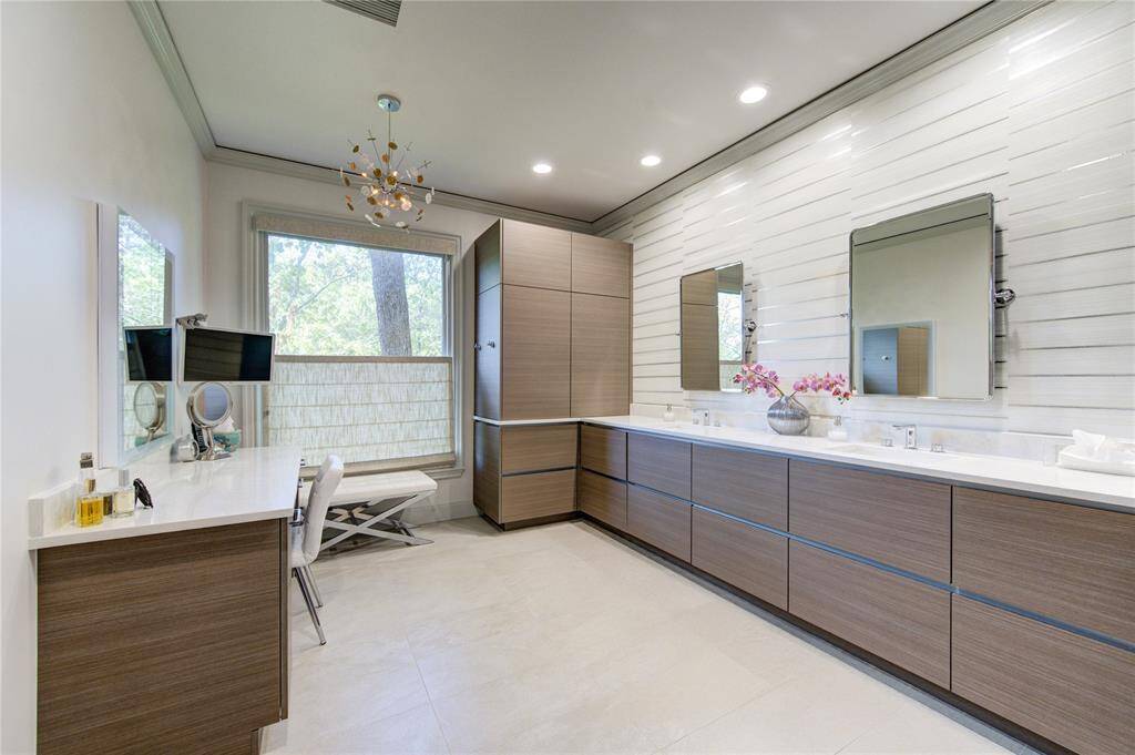 Modern remodeled bathroom featuring sleek wooden cabinetry, separate vanity area, dual sinks, large mirrors, and elegant lighting. The room is bright with natural light from a sizable window, creating a serene, spa-like atmosphere.