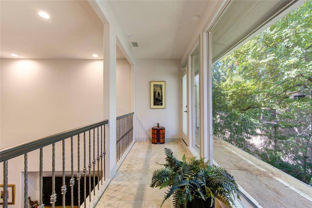 Interior Juliet balcony large windows providing a view of lush greenery. The space features a tiled floor, a decorative railing, and recessed lighting, creating a airy atmosphere.