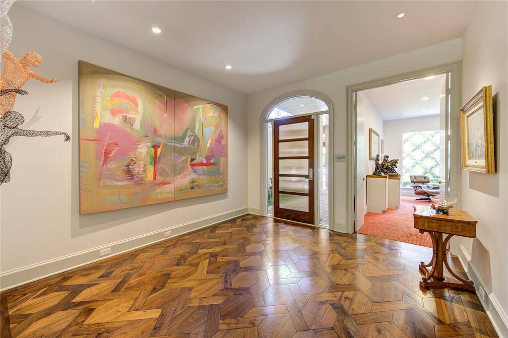 A stylish entryway with elegant wood flooring, Walls for great art and a modern wooden door. The space is well-lit and leads to a bright open library/home office or potential 4th bedroom.