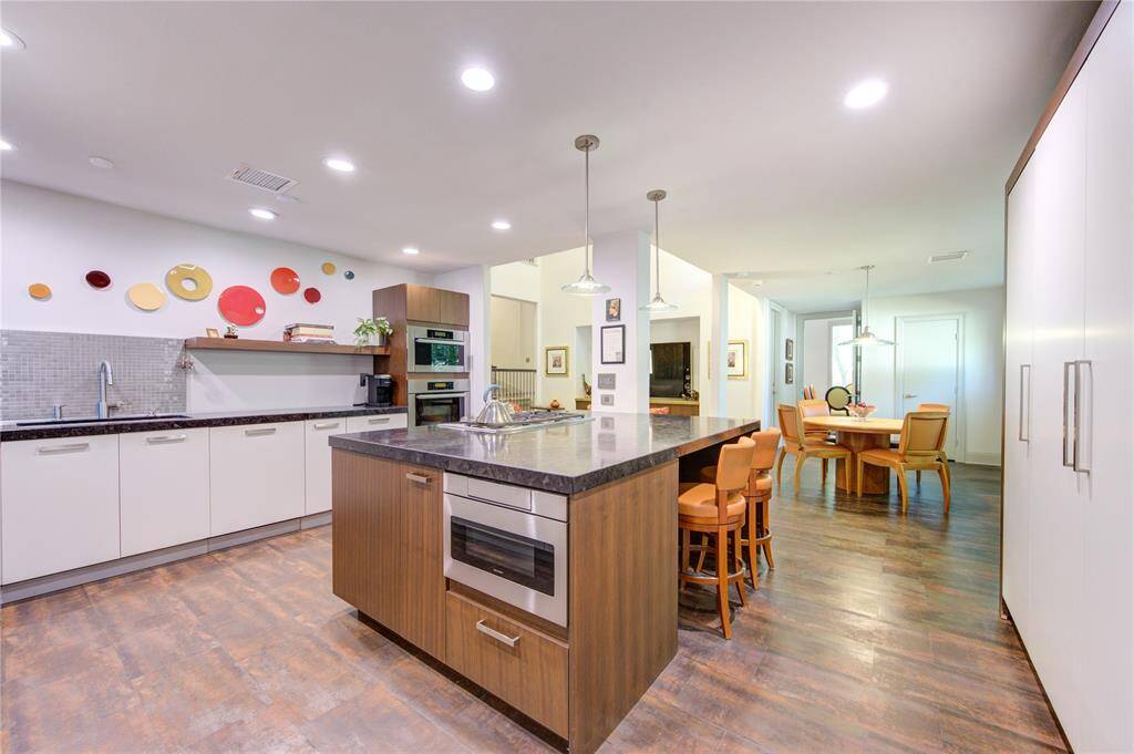 Another view of the kitchen with a large island featuring a built-in oven, steam oven, microwave drawer, and seating area.  There's substantial cabinet space and an open layout leading to a Breakfast area with tile flooring throughout.