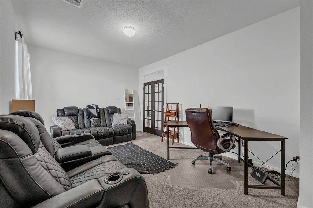This room features comfortable black leather seating, a cozy carpet, and a functional workspace with a desk and chair. French doors add elegance, making it ideal for a home office or media room.
