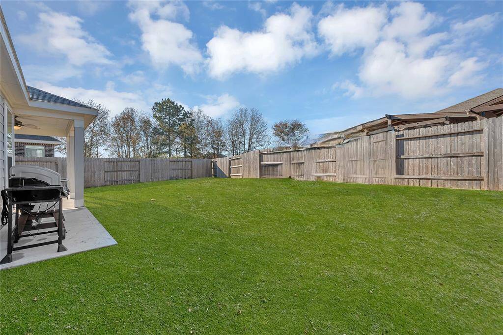 Spacious backyard with a lush green lawn, enclosed by a wooden fence. Features a covered patio area with a grill, perfect for outdoor entertaining.